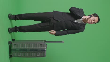 녹색 화면 배경 스튜디오에 서 있는 동안 스마트폰에 대화하는 짐과 함께 아시아 사업가 여행자의 전체 몸