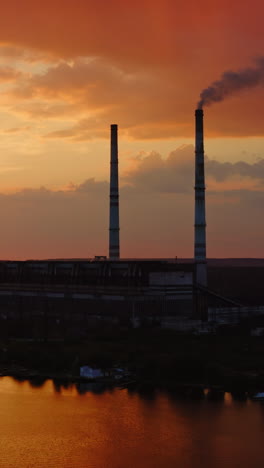 industrial factory. smoke comes from the chimneys of the factory, polluting the atmosphere. video from drone on beautiful sunset. vertical video