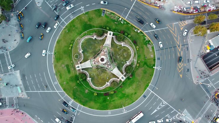 Vista aérea da Plaça d'Espanya em Barcelona mostrando trânsito e pessoas caminhando numa rotatória.