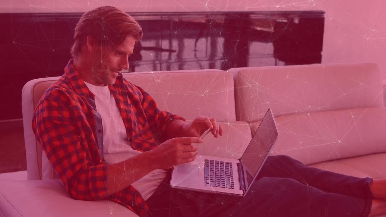Animation of connections over caucasiuan man sitting on sofa and using laptop