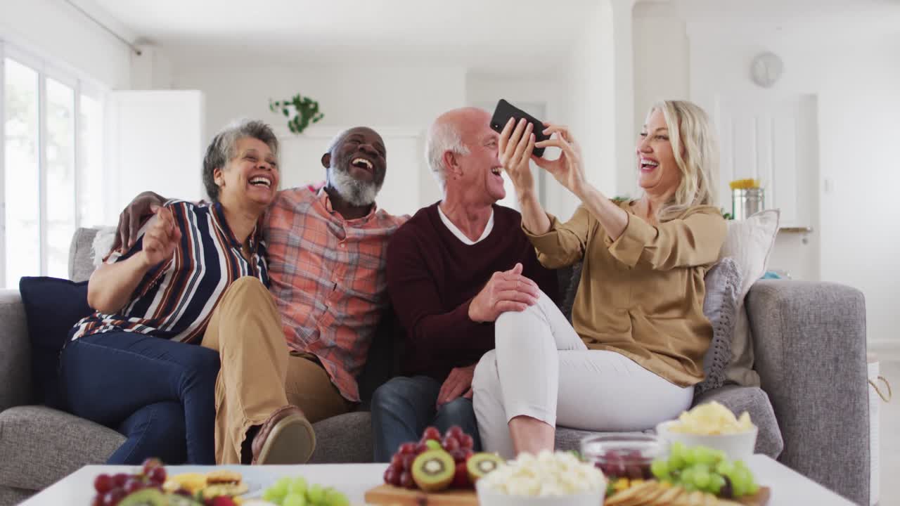 Two diverse senior couples sitting on a couch using a smartphone and laughing