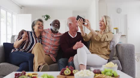 dos parejas mayores diversas sentadas en un sofá usando un teléfono inteligente y riendo