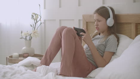 la pequeña amante de la música está escuchando su canción favorita por teléfono inteligente y auriculares en su dormitorio en su tiempo libre el fin de semana