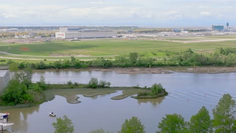 Swamp-Area-With-Moored-Boats-And-Coastal-Heron-Birds-In-The-Forefront-Of-Vancouver-International-Airport-With-Visual-Of-A-Landing-Aircraft-In-Richmond,-BC,-Canada