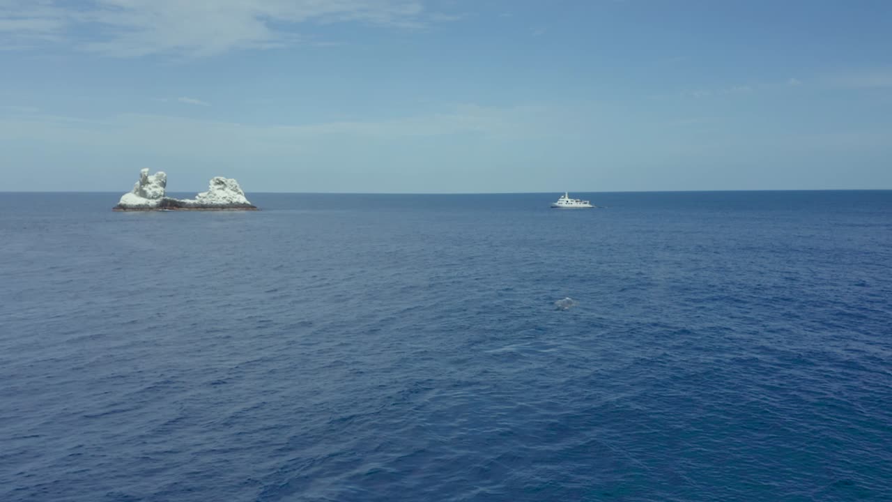 Humpback whale spouts air with dive boat and Revillagigedo Islands in background