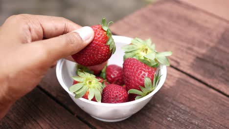hand picking strawberries from a bowl on a wooden table