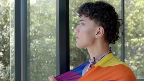 wrapped in pride flag, person standing by window, looking outside thoughtfully