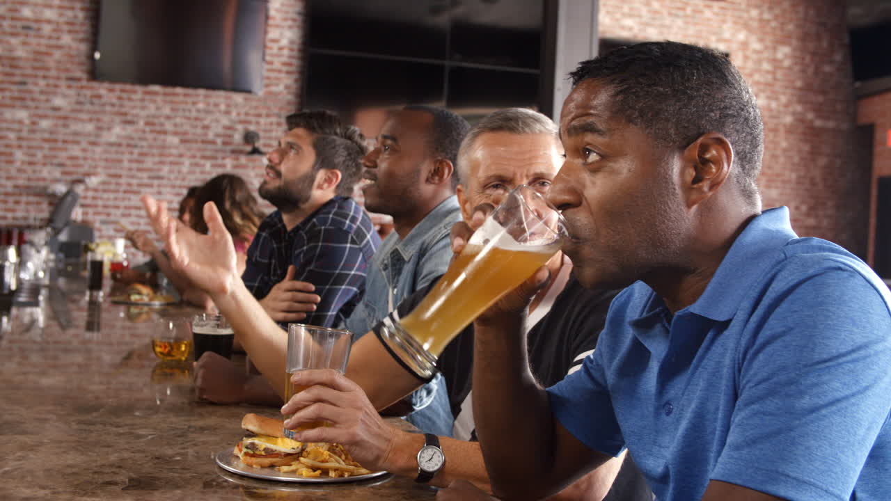 grupo de amigos masculinos viendo un juego en un bar deportivo