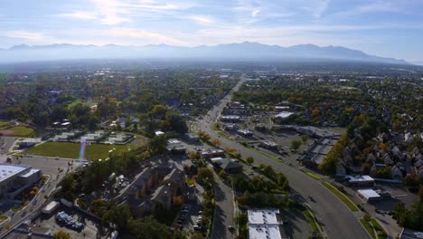 dolly in tilt up aerial drone extreme wide landscape shot of the salt lake county valley covered in buildings, busy roads, and colorful autumn trees surrounded by mountains on a fall evening in utah