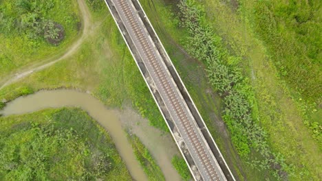 Aerial ascending footage closer from the elevated provincial railway going higher revealing a wider perspective of grassland and water, Muak Klek, Saraburi, Thailand