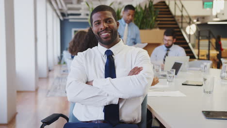 Portrait-Of-Businessman-In-Modern-Office-With-Colleagues-Meeting-Around-Table-In-Background