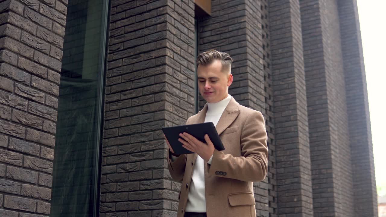 Handsome startup businessman using tablet. Young man texting messages, cheating on his tablet near the office. Business. Social networking
