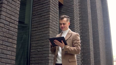handsome startup businessman using tablet. young man texting messages, cheating on his tablet near the office. business. social networking