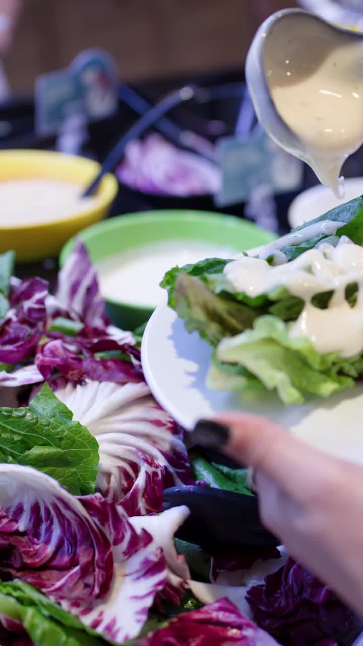 Primo piano di un cliente che versa condimento cremoso su insalata a foglia al buffet self-service