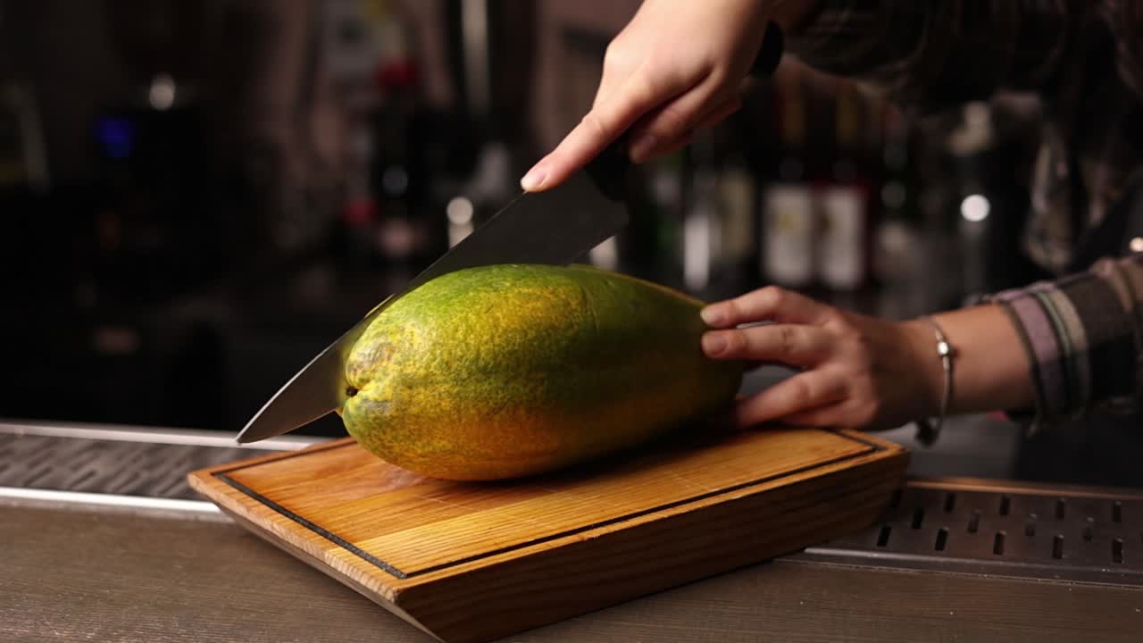 una mujer cortando una papaya en un bar.