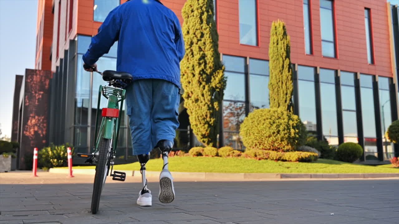 Slow motion view of a man with prosthetic legs. Walking with a bicycle on the street with greenery