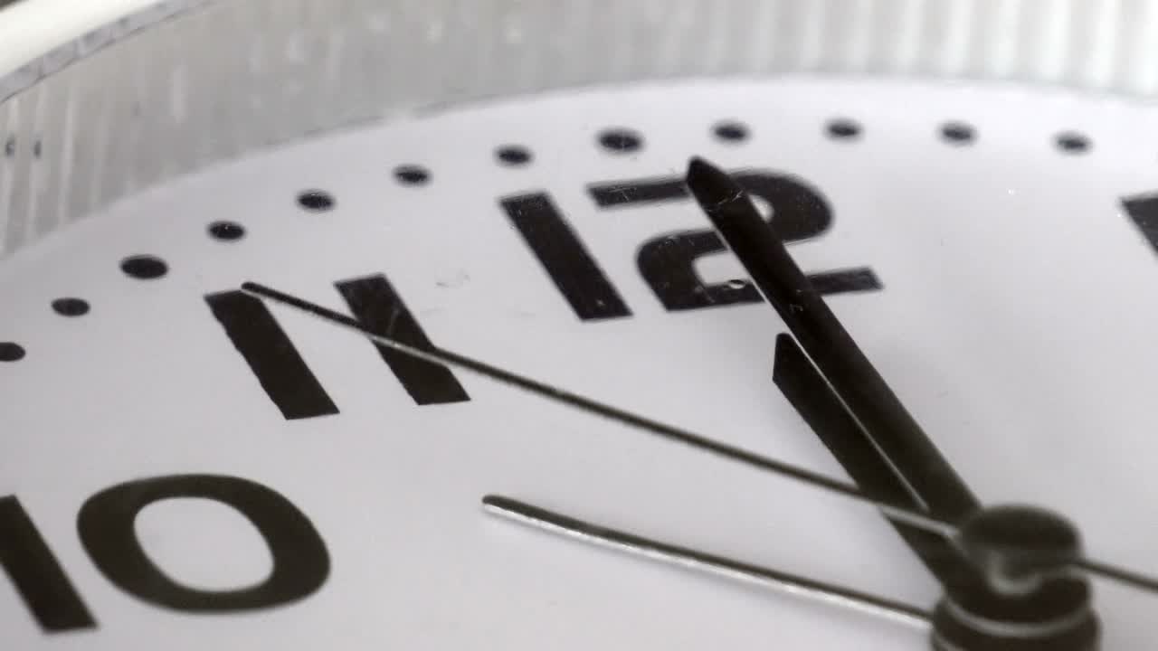 Circular wall clock ticking towards 12 o'clock