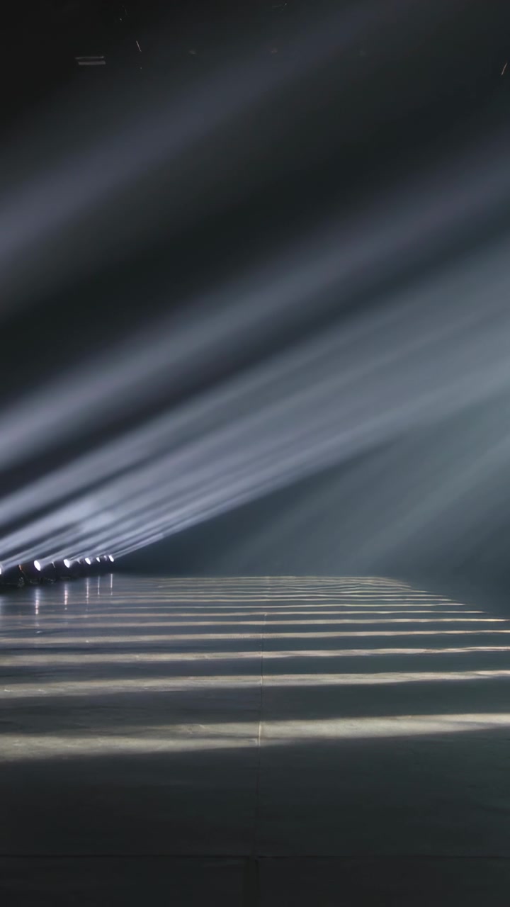 Video verticale: Lampade di segnalazione che proiettano fasci di luce angolati, creando un pavimento a strisce sul palco per le prove, con nebbia.