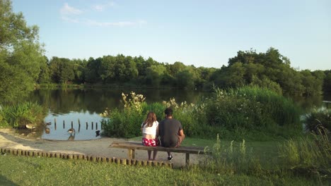 una pareja sentada en un banco frente a un lago con gansos al atardecer