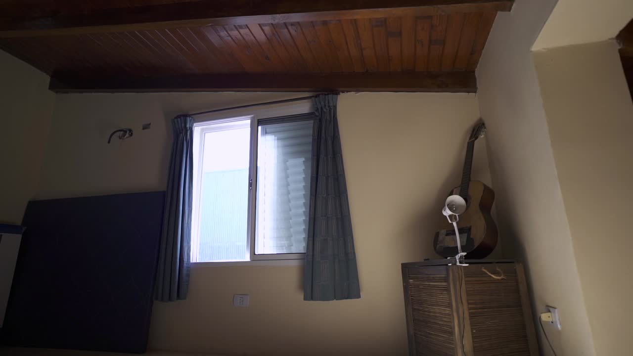 Minimalist room with warm wooden ceiling, white walls, and practical storage. Window provides natural light. Ideal for rental listings.