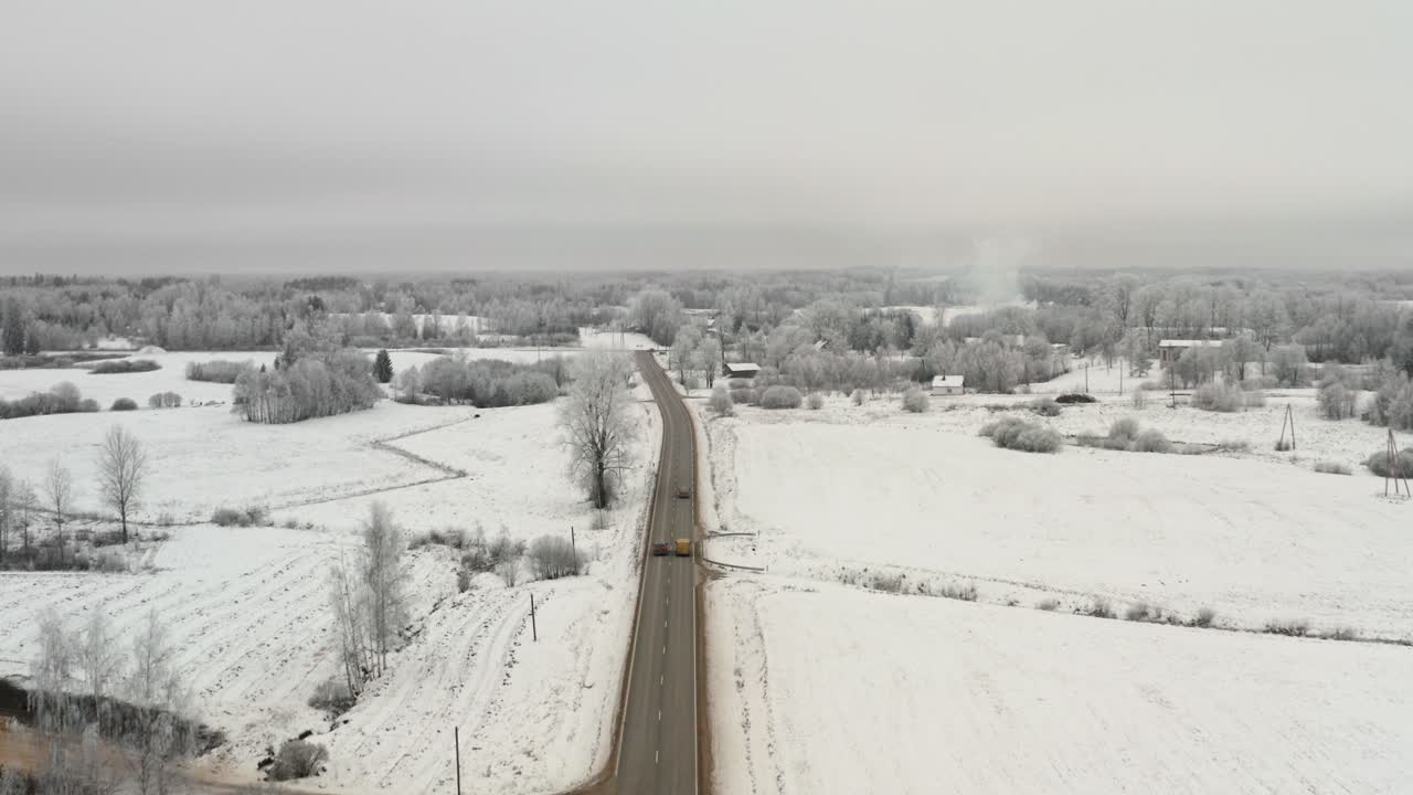 Aerial drone view of a straight countryside road with one car overtaking another one. Frozen winter weather with lots of snow.