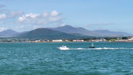 Weißes-Schnellboot-Inmitten-Der-Atemberaubenden-Schönheit-Eines-Sonnigen-Tages-Mit-Wolken,-Eingerahmt-Von-Den-Majestätischen-Mourne-Mountains-In-Nordirland