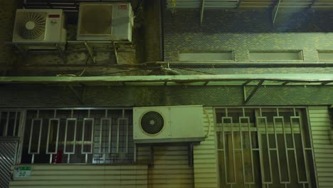 old vintage ac unit fan on side of apartment building in asia at night