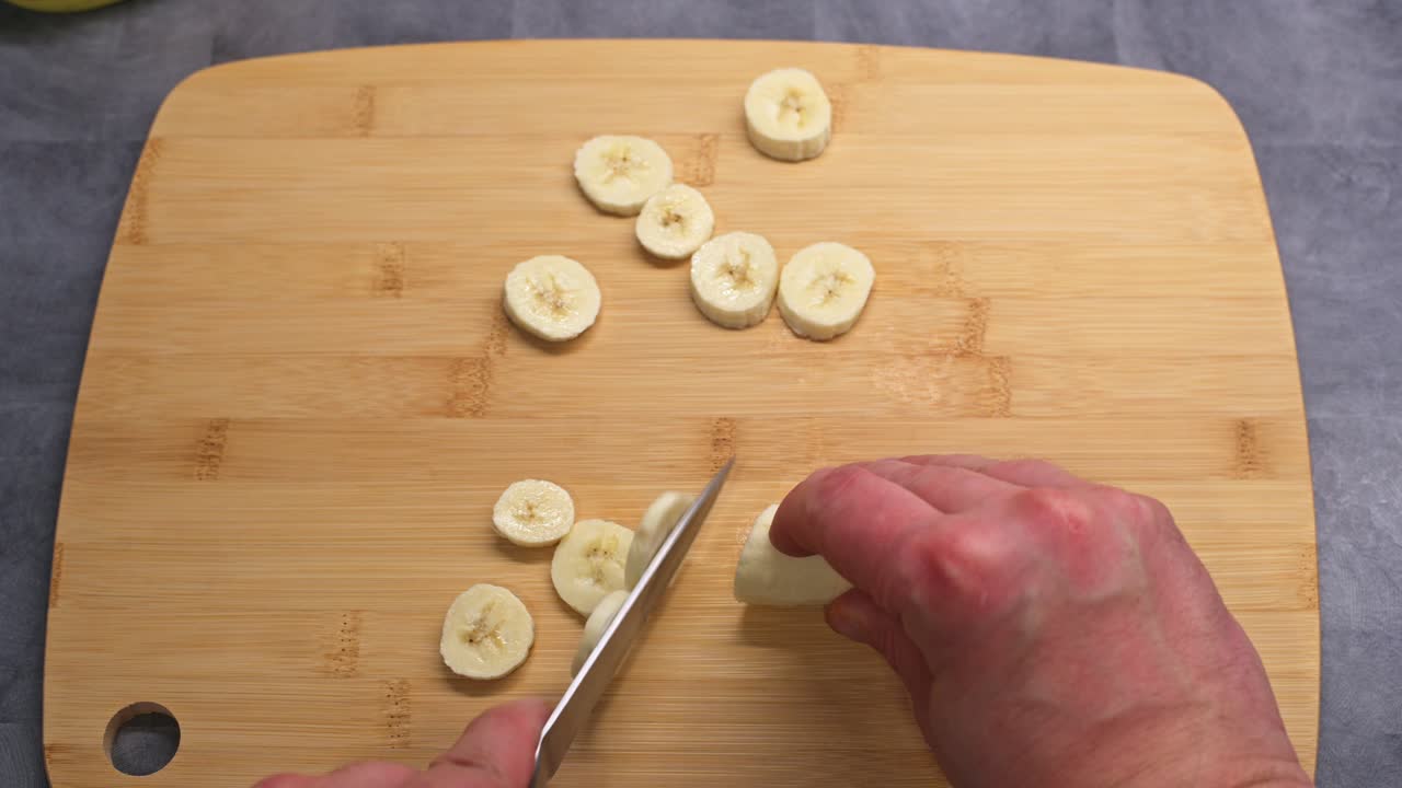 A close-up video of a person slicing a fresh banana on a wooden cutting board.