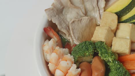 close up of a bowl of sukiyaki or shabu spinning around on the white table