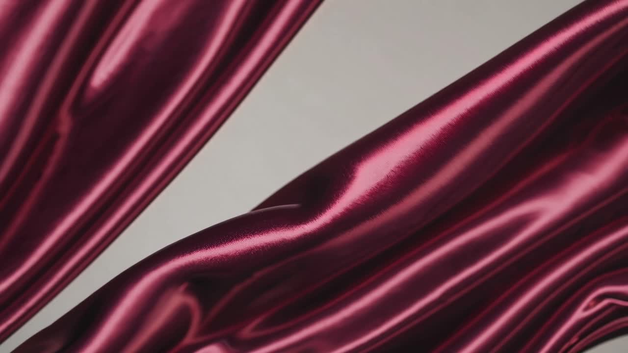Close-up video of flowing burgundy silk fabric, showcasing its smooth texture and elegant drape