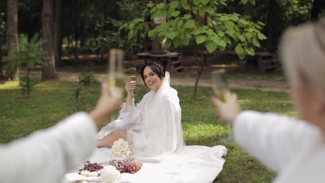 novia en vestido de boudoir sentada en el jardín de la mañana bebiendo champán mujer en velo de vestido de noche