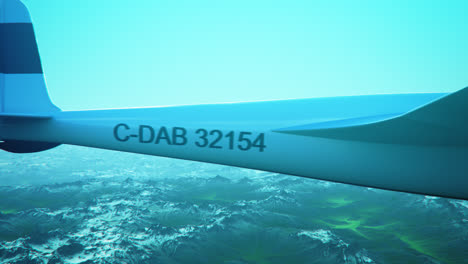 an aerial view of the white sailplane with no propeller calmly gliding in the sky, over snow-covered mountains. flying aerodynamic aircraft is a great way of spend leisure time.