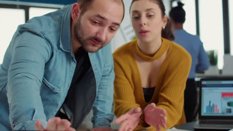 Team-of-two-coworkers-looking-at-tablet-with-data-charts-on-desk-and-talking-about-business-strategy