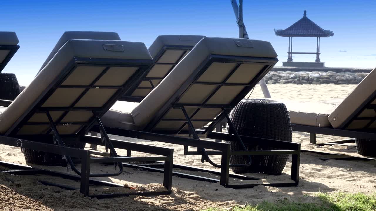 las olas del mar cálido corren en la playa de arena del complejo tropical con sombrillas y sillones