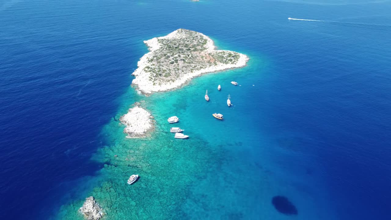 Aerial view showing heart shaped island surrounded by anchored boats, turquoise water, rocky vegetation, and calm coastal scenery creating peaceful marine atmosphere around Kekova Bay in Antalya