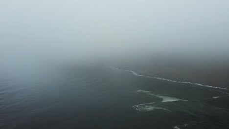 a drone shot strafing and exiting a low cloud ceiling revealing the bir sur coastline with turquoise pacific ocean saltwater with waves crashing against cliffs off the historic highway 1