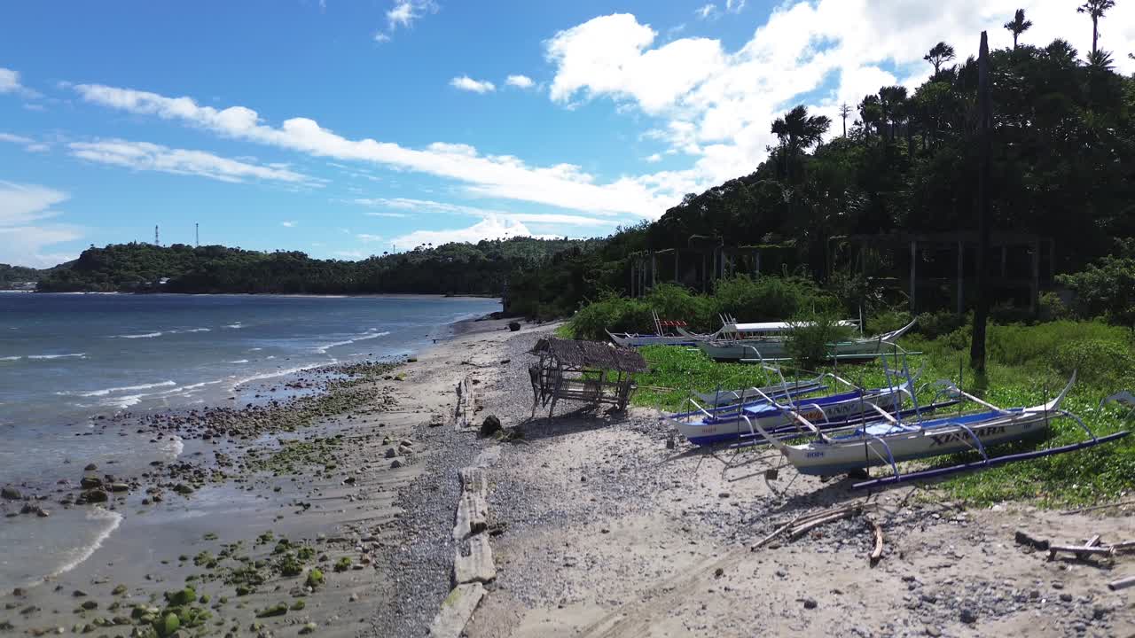 Rekaman drone udara dari perahu yang bersandar di Pantai Aninuan di Puerto Galera, Filipina dengan air sebening kristal, pantai berpasir, hutan lebat, dan pegunungan hijau di latar belakang yang membentuk lanskap tropis