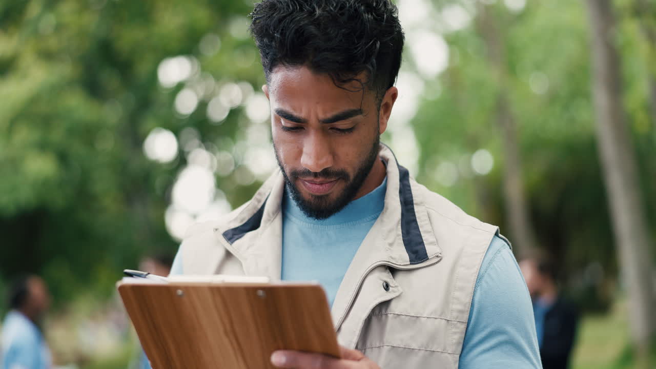 Young Man Writing on Clipboard Outdoors in a Park