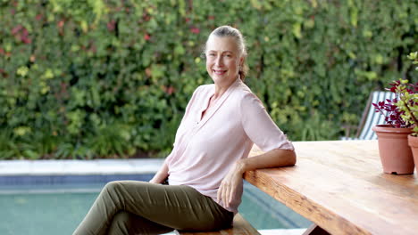 smiling senior woman sitting on bench by pool, enjoying outdoor relaxation