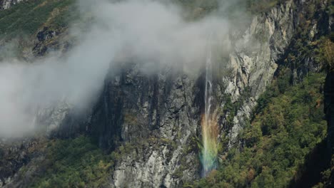 the gjerdefossen waterfall in geiranger flows down rocky cliffs, with sunlight casting a colorful rainbow in the mist