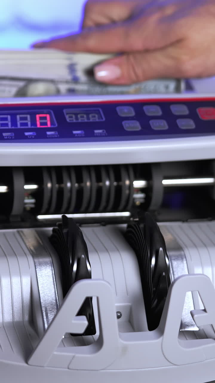 Electronic equipment for financial operations in bank. Woman's hand putting paper money into a counting machine. Vertical video