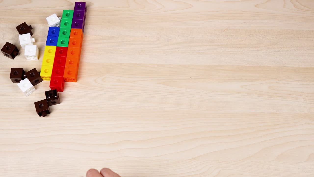 Hands manipulate colorful cubes on a wooden surface
