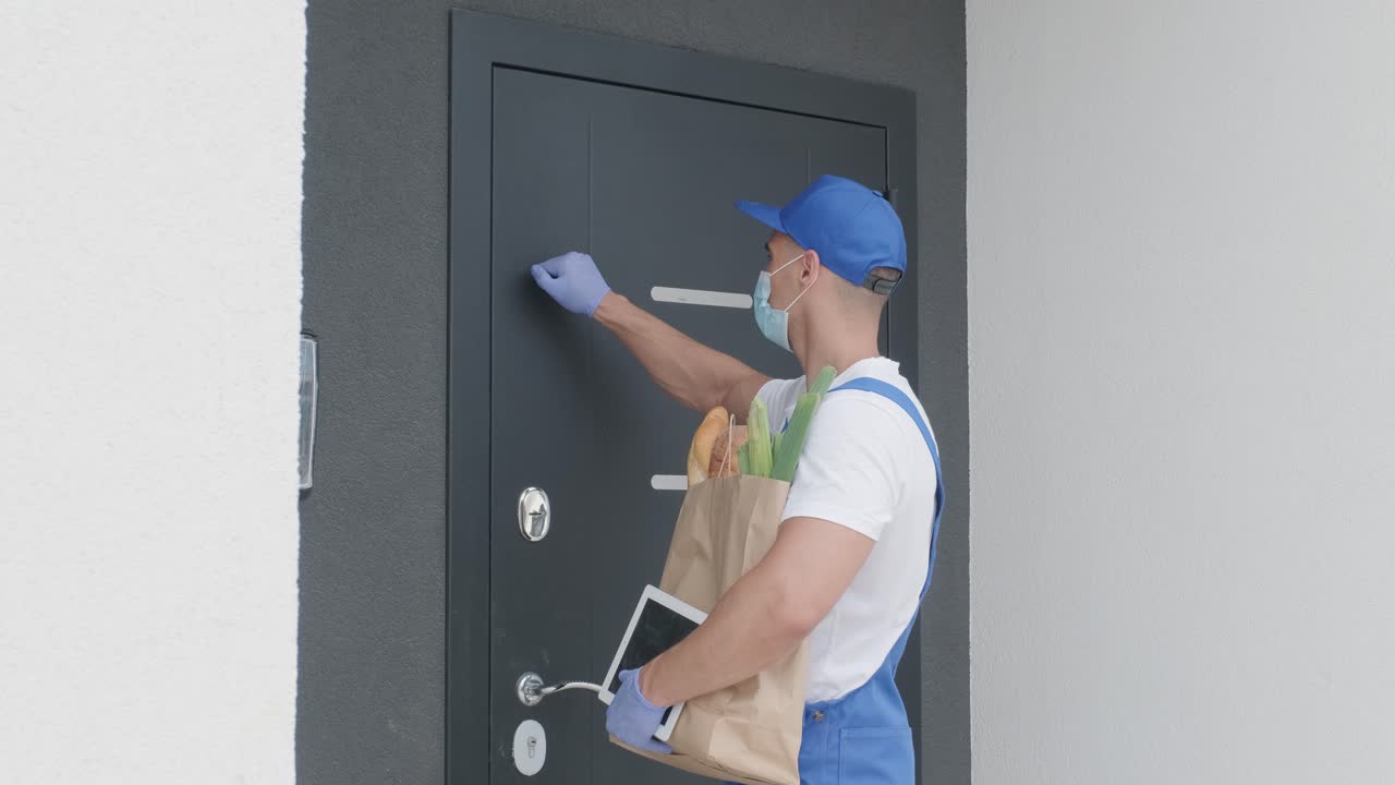 joven mensajero con máscara de protección y guantes entrega un paquete de compras con alimentos directamente a casa de un cliente con seguridad. entrega de alimentos, entrega a casa en cuarentena