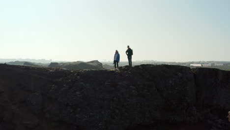 Aerial-birds-eye-view-two-hikers-standing-on-top-of-cliff-in-Iceland.-Drone-view-two-male-backpackers-enjoying-landscape-standing-on-top-of-a-hill-looking-panorama