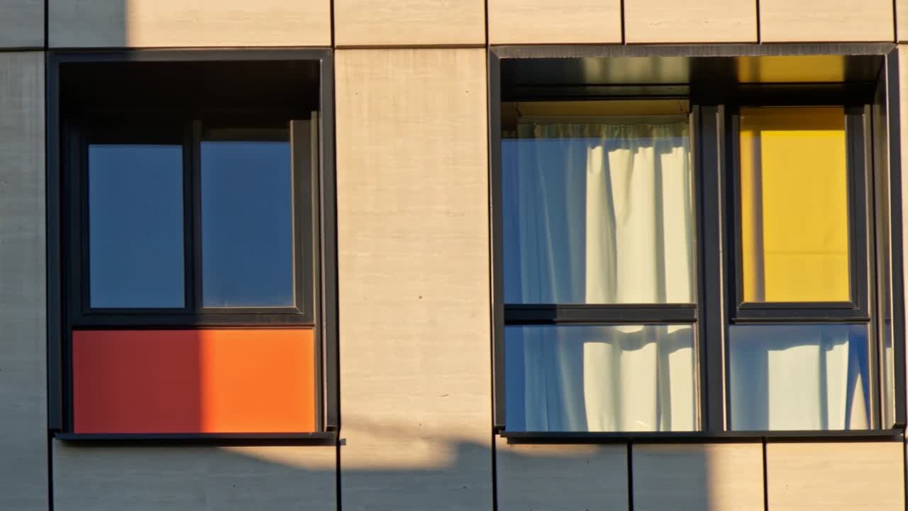 Panning camera across building facade to right after pause, to show orange panel and yellow blind