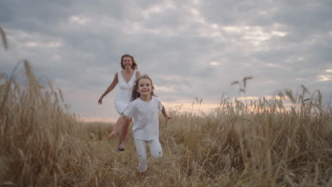 daughter and mother dream together run in the wheat field at sunset. happy family people in the wheat field concept. mom and girl playing catch-up run. baby child fun running in green meadow.