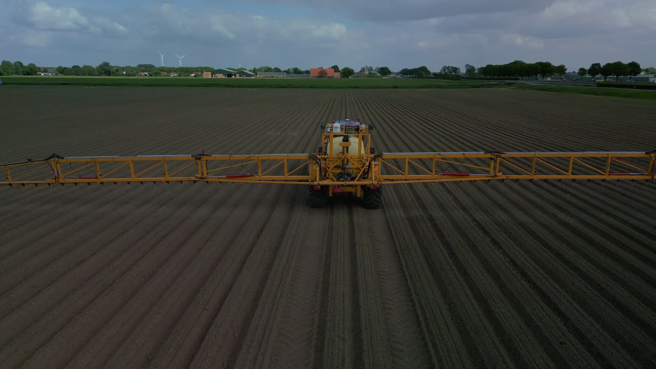 Farmer on tractor spraying field with crop protection products drives away from camera