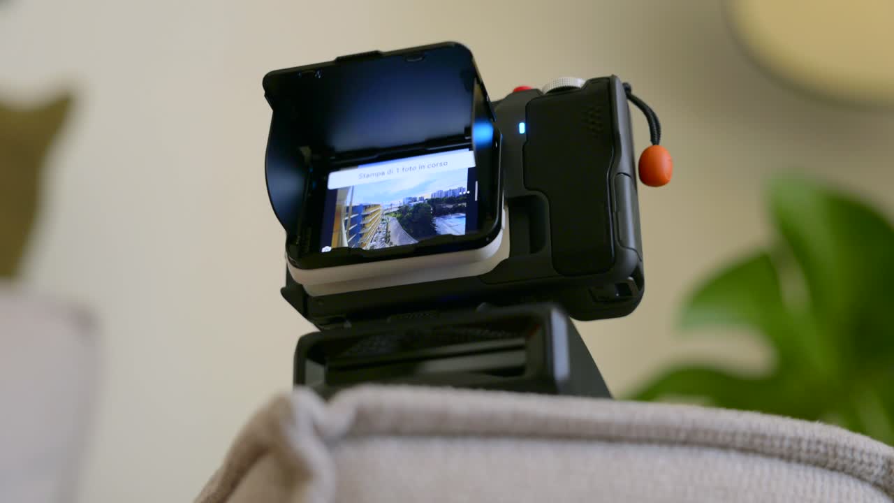 Primo piano di una action camera a 360 gradi con schermo orientabile su un piccolo treppiede in interni. Un dito scorre la riproduzione sul touchscreen.