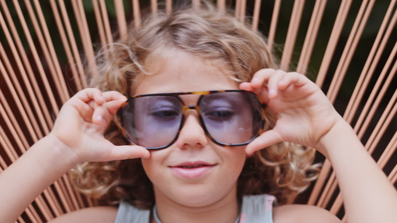 Cool little girl in a garden chair with sunglasses making faces