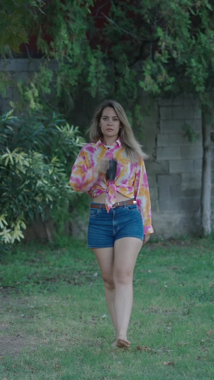Woman in tie dye shirt drinking from cup outdoors